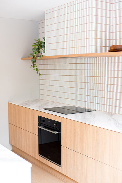Kitchen with a white marble benchtop blending into the white tiled wall behind.